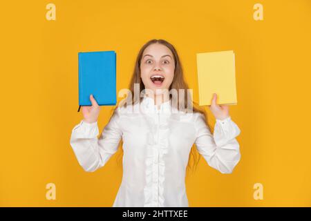 stupito teen ragazza che presenta libro di lavoro della scuola su sfondo giallo, istruzione Foto Stock