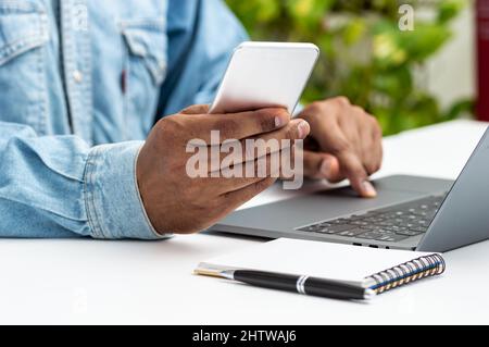 Primo piano di un uomo con le mani utilizzando uno smartphone e un computer portatile su un desktop a casa o in ufficio Foto Stock