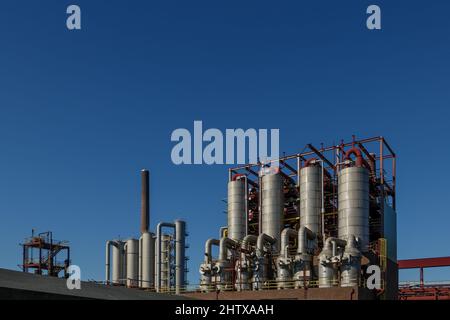 vista soleggiata all'aperto dell'alto serbatoio di raffineria in metallo, struttura verniciata di rosso e tubazioni in acciaio contro il cielo blu nella miniera di carbone o nell'area chimica industriale. Foto Stock