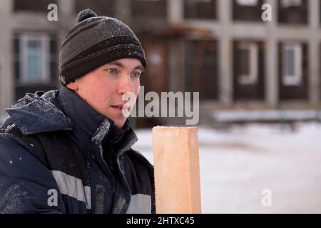 Builder in una giacca blu con cappuccio e un asse in mano al cantiere della città di ghiaccio Foto Stock