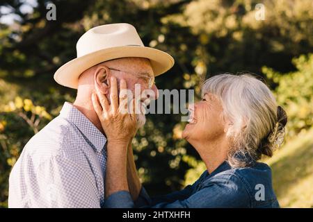 Coppia anziana allegra sorridente l'un l'altro con amore e affetto. Coppia dai capelli grigi che condivide un momento romantico mentre si trova in un parco. Buon eld Foto Stock