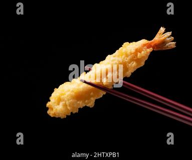 Tempura di gamberi sollevata con bacchette contro uno sfondo nero. La tempura è un cibo giapponese. Si tratta di gamberi fritti giapponesi. Foto Stock