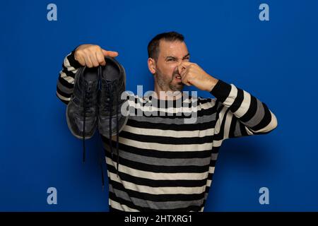 Un uomo tiene le sneakers nelle sue mani. Odore sgradevole. Gambe puzzolanti, funghi sulle gambe. Foto Stock