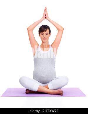 Calma e tranquillità per mamma e bambino. Una giovane donna in attesa meditando pacificamente mentre è isolata su bianco. Foto Stock