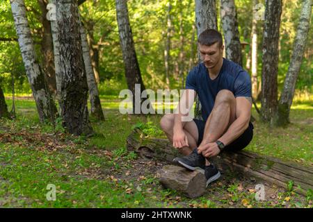 L'uomo che lega le sue scarpe nel parco all'aperto, intorno alla foresta, querce verde erba verde giovane atleta resistente atleta. Sano runner foresta Foto Stock