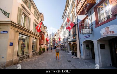 Turista in Augustinergasse, vicolo con case storiche e bandiere svizzere nel centro storico, Zurigo, Svizzera Foto Stock