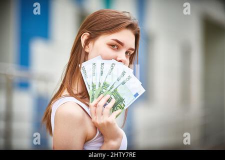 concetto di gente - ragazza sorridente adolescente in pullover che tiene centinaia di banconote in euro su sfondo grigio Foto Stock