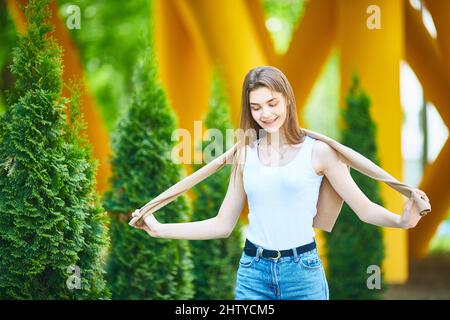 giovane adolescente che cammina lungo la strada in jeans e un maglione in una giornata estiva. Il concetto di moda giovanile. Stile di vita urbano. Foto Stock