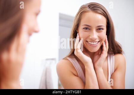 Ceneri la fede di tutti. Una giovane donna che tocca il viso felicemente mentre guarda nello specchio. Foto Stock