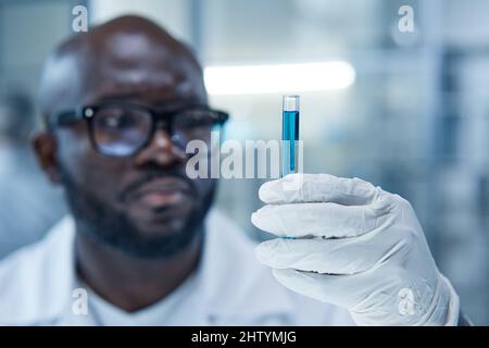 Primo piano di un matraccio di conservazione per scienziato africano con campione in guanti protettivi durante l'esperimento medico in laboratorio Foto Stock