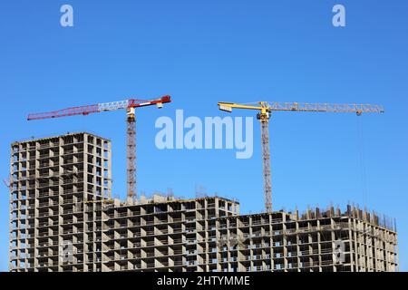 Costruzione torre gru sopra edificio residenziale incompiuto su sfondo cielo blu. Edilizia abitativa, condominio Foto Stock