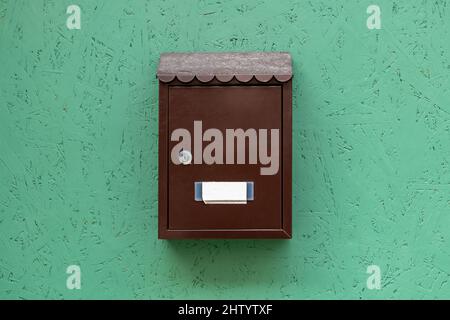 Un unico semplice appartamento chiuso a chiave letterbox con un vuoto nome tag, classico tradizionale residenza mailbox appeso su una parete verde, posta in metallo l Foto Stock