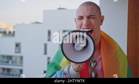 persona non binaria che urla in ager e combatte per i loro diritti con bandiera arcobaleno sulle spalle. Foto di alta qualità Foto Stock