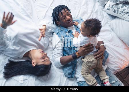 Giovane famiglia multirazziale che si stende su fogli bianchi, godendo il loro tempo libero, e trascorrendo il tempo insieme. Foto di alta qualità Foto Stock