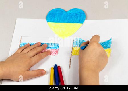 Le mani dei bambini di un bambino tirano le bandiere di primo piano di Ucraina e Russia. Vista dall'alto. Bambini contro la guerra. I bambini disegnano per la pace dentro Foto Stock