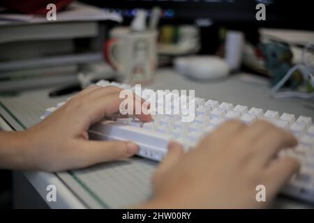 Primo piano digitazione rapida sulla tastiera. Corpo parti mani e dita in movimento. Ufficio disordinato con molti oggetti che si infilano sul tavolo. Ufficio moderno con molti Foto Stock