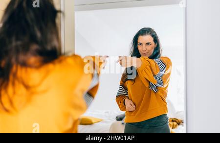 Donna singola sicura di sé che punta il dito alla sua riflessione nello specchio, ballando e flelling buono. Persona indipendente con alta autostima parla posi Foto Stock
