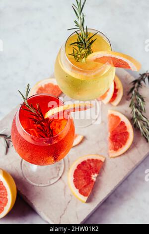 Rosso e bianco aperol spritz guarnire in bicchieri da vino con rosmarino e pompelmo su un lussuoso tavolo in marmo. Cocktail di alcol amaro in wineglass. Foto Stock