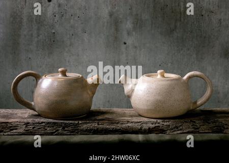 Due bollitore artigianale in teiera in ceramica fatto a mano per la cerimonia del tè in piedi su un vecchio ripiano in legno con parete grigia sullo sfondo Foto Stock