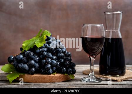 Decanter di vetro e bicchiere di vino con vino rosso e uva fresca su tavola di legno. Foto Stock