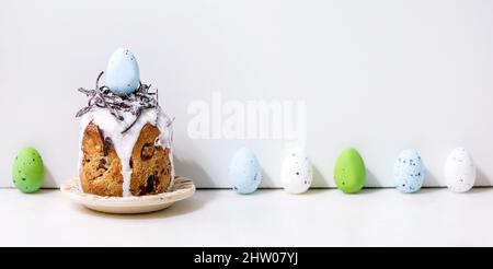 Torta tradizionale di Pasqua fatta in casa con nido di cioccolato, uova sul piatto in piedi su tavola bianca con uova colorate in fila. Tradizionale easta ortodossa Foto Stock