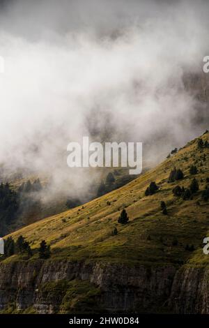Pendii di montagna tagliati in verticale coperti di erba verde e vegetazione sotto le nubi nubi nebbie Foto Stock