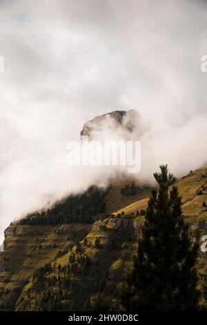 Pendii di montagna tagliati in verticale coperti di erba verde e vegetazione sotto le nubi nubi nebbie Foto Stock