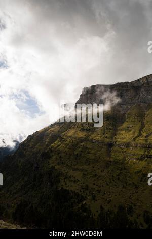 Pendii di montagna tagliati in verticale coperti di erba verde e vegetazione sotto le nubi nubi nebbie Foto Stock