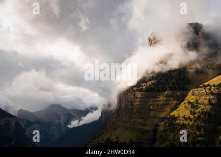Pendii di montagna tagliati in verticale coperti di erba verde e vegetazione sotto le nubi nubi nebbie Foto Stock