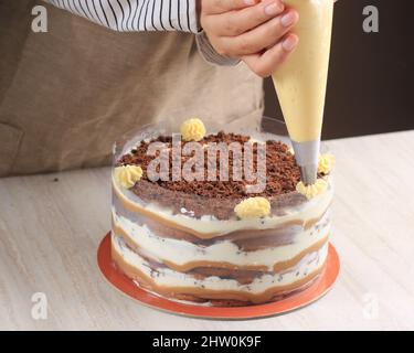 Donna asiatica mano decorando Tiramisu con Swirl Mascarpone utilizzando la borsa per tubazioni, facendo Tiramisu torta intera Foto Stock