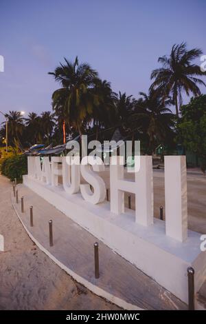 Lettere di pietra bianca per la designazione dell'isola di Maafushi con le palme di Nizza durante il tempo del tramonto, Maldive Foto Stock