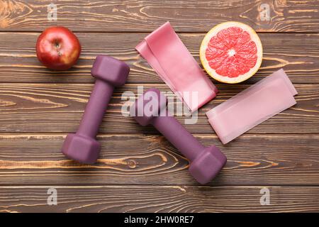 Manubri eleganti, frutta e fasce elastiche su sfondo in legno Foto Stock