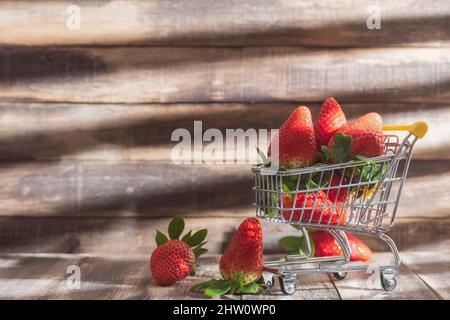 Fragole fresche in un carrello su sfondo di legno. Un sacco di fragole dolci mature in un cestino. Primo piano. Vista laterale e spazio per il testo Foto Stock