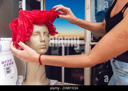 testa mannequin su un tavolo accanto alla finestra con un bel cappello rosso vintage femmina, designer arrangiando i dettagli del cappello vintage posto sul ma Foto Stock