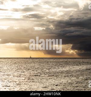 Uno yacht naviga nella baia di Tamarin, al largo della costa sud-occidentale di Mauritius. Le nuvole di pioggia si trovano nel cielo altrimenti dorato sopra l'Oceano Indiano. Foto Stock