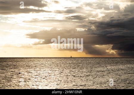 Uno yacht naviga nella baia di Tamarin, al largo della costa sud-occidentale di Mauritius. Le nuvole di pioggia si trovano nel cielo altrimenti dorato sopra l'Oceano Indiano. Foto Stock