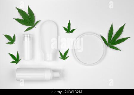 Creme cutanee a base di canapa. Cosmesi di canapa naturale. Tubi cosmetici in plastica bianca per crema e olio con foglie di canapa su sfondo bianco, mock up, lat Foto Stock