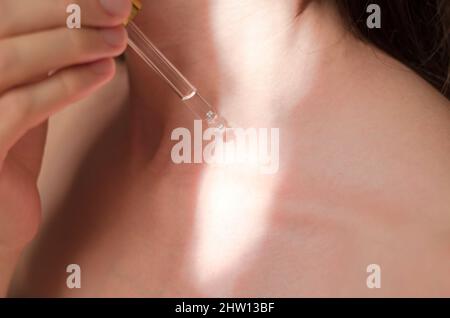 Concetto di terapia cosmetica. Una donna applica olio al suo corpo. Una goccia di olio essenziale gocciola da una pipetta sul corpo di una donna. Siero corporeo. Processo cosmetico Foto Stock