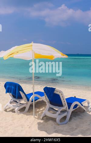 Due chaise lounge in plastica blu sotto l'ombrello giallo sulla spiaggia locale di Bikini dell'Isola Maafushi, Maldive Foto Stock