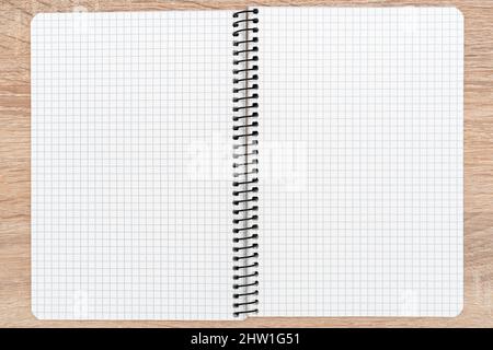 Aprire il notebook bianco con rilegatura a spirale e righe quadrate con spazio per le copie su una scrivania in legno, vista dall'alto Foto Stock