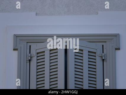 Casa neoclassica grigio chiaro finestra in legno con persiane su una parete bianca a Nafplio, Grecia. Foto Stock