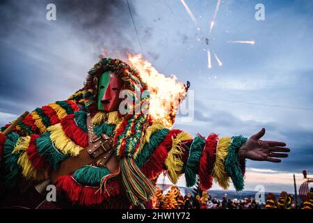 Caretos esegue rituali religiosi durante l'incendio di Entrudo (un carito gigante) durante la celebrazione del Carnevale di Podenza. Nel villaggio portoghese di Podence, nel comune di Macedo de Cavaleiros, durante il carnevale, gli uomini indossano il costume tradizionale, noto come 'Caretos', indossano maschere in ottone o legno e indossano colorati costumi di lana. Urlano e inseguono le persone per strada per spaventarle, specialmente le donne single. Caretos de Podence è stato dichiarato patrimonio culturale immateriale dell'umanità dall'UNESCO il 2019 dicembre. L'evento si conclude con l'incendio di Entrendo (un carato gigante). Foto Stock