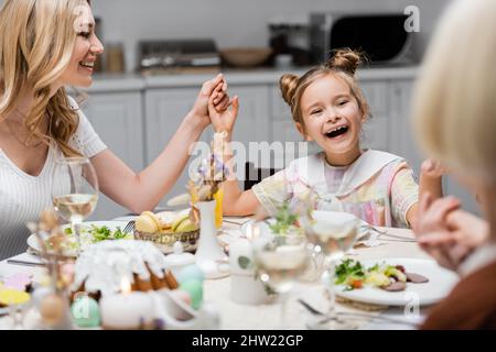 ragazza stupita che tiene le mani con la madre e nonna vicino cena di festa sul tavolo della cucina, immagine di scorta Foto Stock