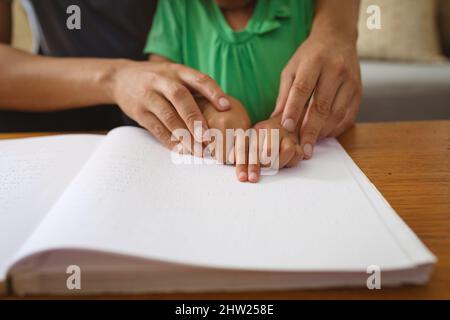 Metà sezione del padre biraciale che aiuta figlia cieca a studiare mentre legge il libro con il braille Foto Stock