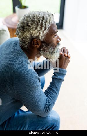 Vista laterale di un uomo alto afroamericano barbato con mani sul mento che pensa in salotto a casa Foto Stock