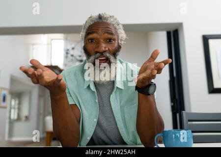 Ritratto di sorprendo uomo anziano afroamericano gesturing mentre si siede in soggiorno a casa Foto Stock
