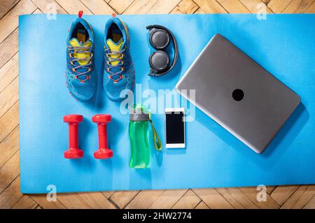 Scarpe sportive e attrezzature per il fitness. Attrezzature fitness e un computer portatile. Fitness a casa. Foto Stock