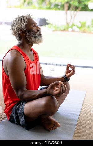 L'anziano afroamericano con gli occhi ha chiuso meditando mentre praticano lo yoga a casa Foto Stock