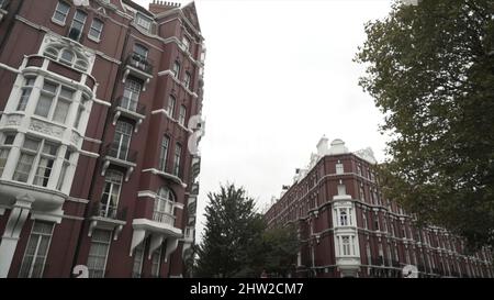 Un tipico edificio di mattoni rossi londinesi, Inghilterra, vista dal basso. Architettura cittadina, strada con case incredibili e alberi verdi su sfondo cielo nuvoloso. Foto Stock