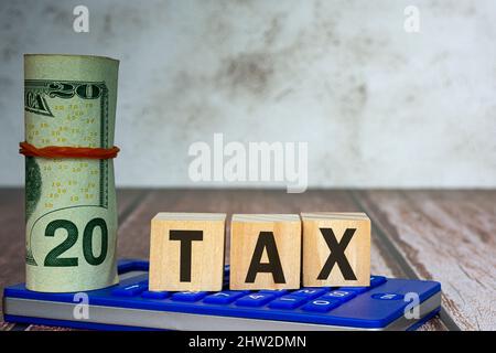 Testo delle imposte sul cubo in legno Alphabet su una calcolatrice blu con banconote su un banco in legno. Concetto aziendale e fiscale. Foto Stock